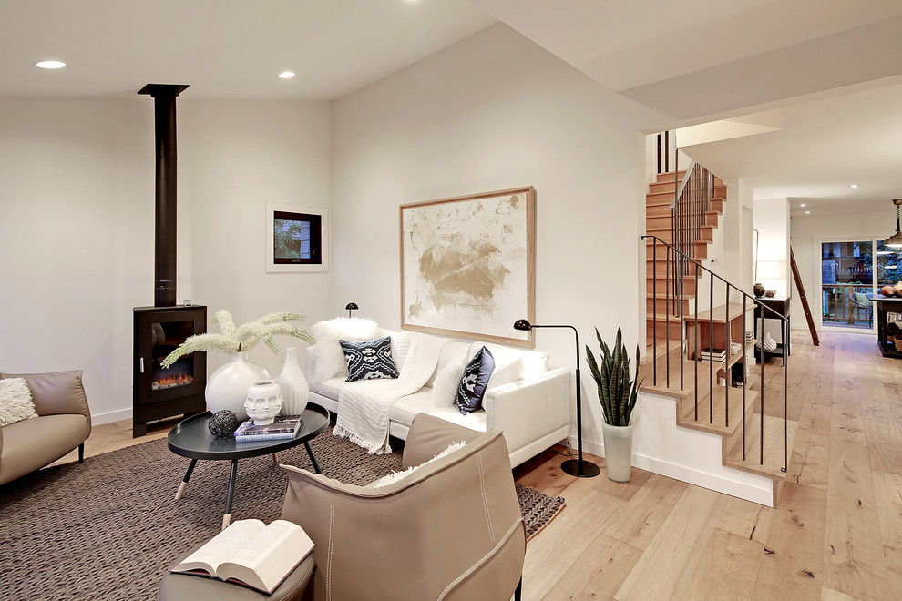 Пример оригинального дизайна: открытая гостиная комната в стиле неоклассика (современная классика) с белыми стенами, светлым паркетным полом и печью-буржуйкой без телевизора