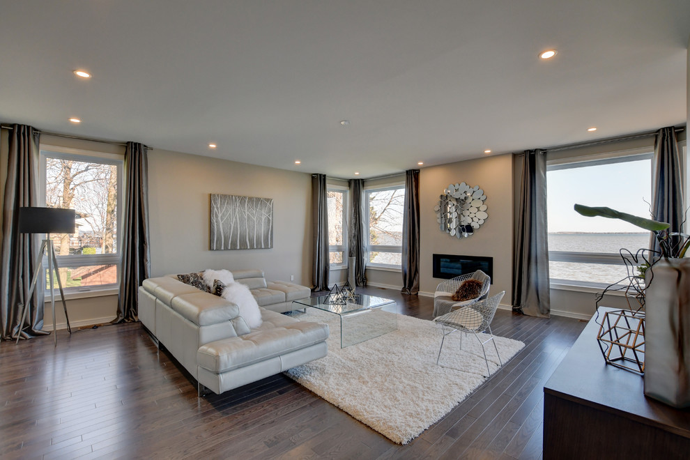 Immagine di un grande soggiorno minimal aperto con pareti beige, pavimento in legno massello medio, camino classico e TV a parete