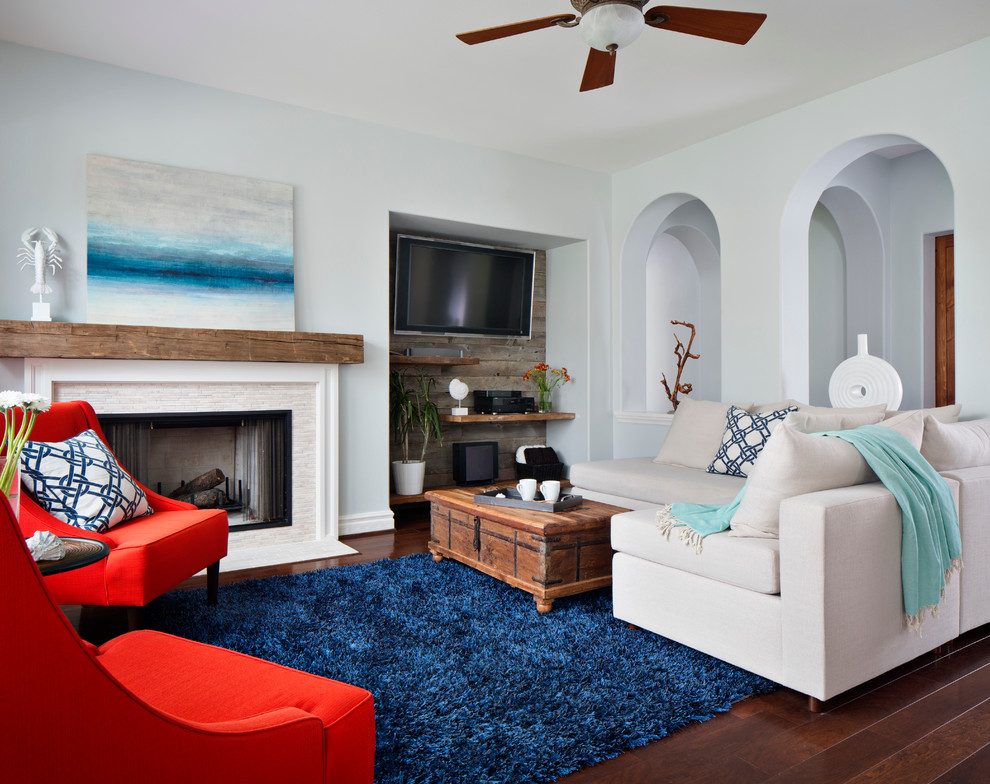 Пример оригинального дизайна: открытая гостиная комната среднего размера в морском стиле с синими стенами, стандартным камином, телевизором на стене, паркетным полом среднего тона, с книжными шкафами и полками и фасадом камина из камня