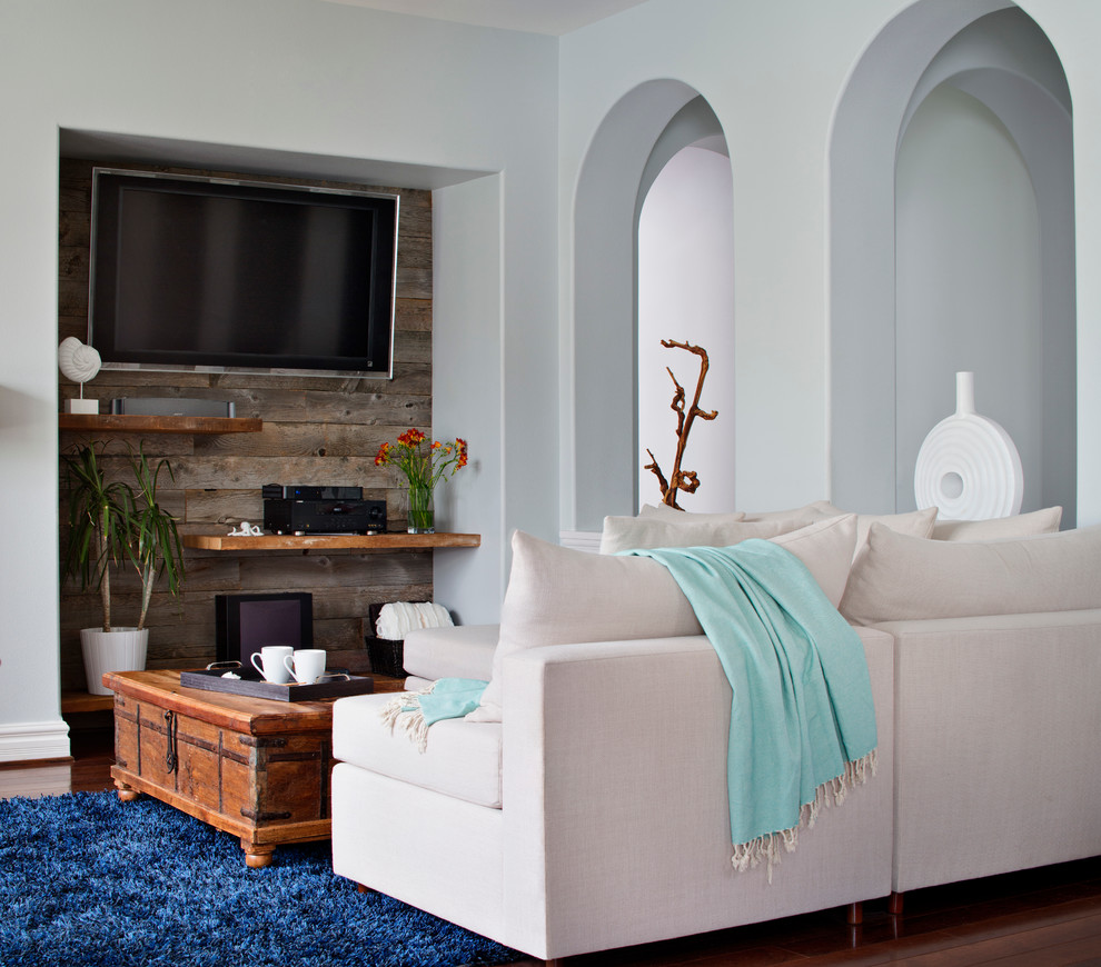 На фото: открытая гостиная комната среднего размера в морском стиле с паркетным полом среднего тона, телевизором на стене, с книжными шкафами и полками, синими стенами, стандартным камином и фасадом камина из камня с