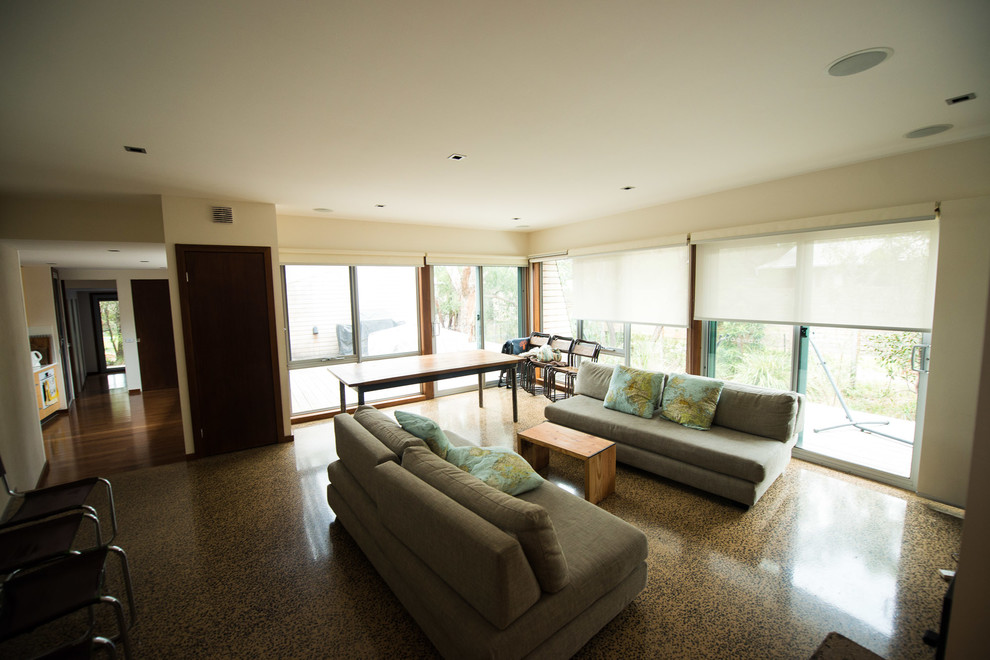 Стильный дизайн: большая открытая гостиная комната в современном стиле с белыми стенами, бетонным полом, печью-буржуйкой, фасадом камина из металла и телевизором на стене - последний тренд