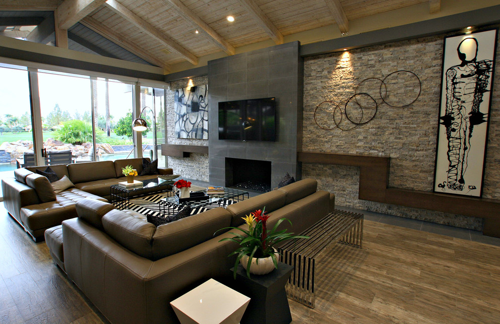 This is an example of a large contemporary open plan living room in Los Angeles with medium hardwood flooring, a standard fireplace, a tiled fireplace surround, a wall mounted tv and brown floors.
