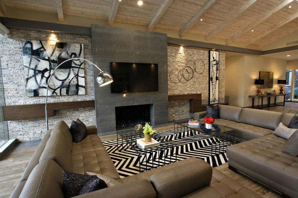 Imagen de salón abierto contemporáneo grande con suelo de madera en tonos medios, todas las chimeneas, marco de chimenea de baldosas y/o azulejos, televisor colgado en la pared y suelo marrón