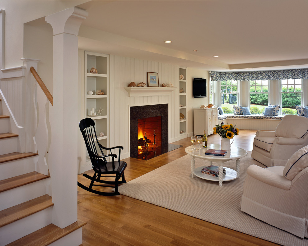 Immagine di un soggiorno stile marinaro con pareti bianche, pavimento in legno massello medio, camino classico e TV a parete
