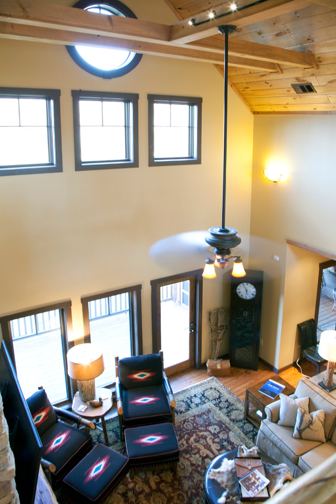 Источник вдохновения для домашнего уюта: двухуровневая гостиная комната среднего размера в стиле рустика с бежевыми стенами, паркетным полом среднего тона, стандартным камином, фасадом камина из камня и телевизором на стене