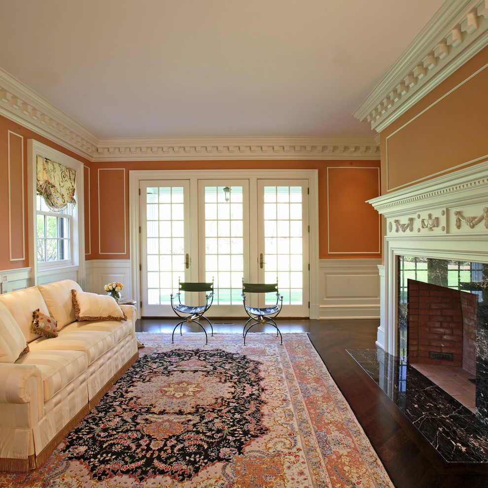 Стильный дизайн: парадная, открытая гостиная комната в классическом стиле с оранжевыми стенами, темным паркетным полом, стандартным камином и фасадом камина из штукатурки без телевизора - последний тренд