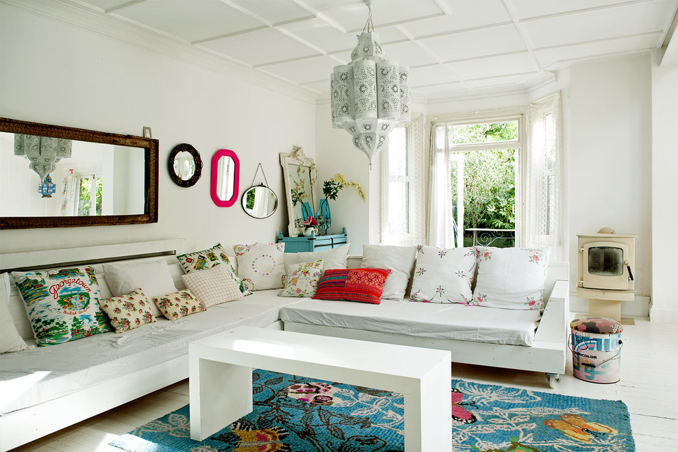 На фото: гостиная комната в стиле фьюжн с белыми стенами, деревянным полом, печью-буржуйкой и эркером с