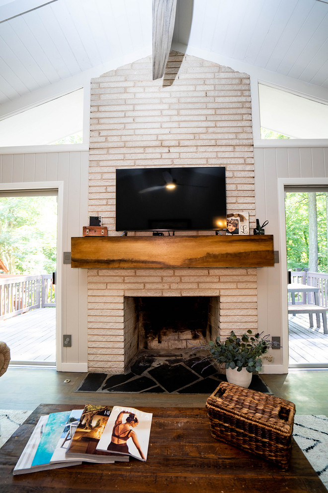 アトランタにある低価格の中くらいなミッドセンチュリースタイルのおしゃれな独立型リビング (標準型暖炉、壁掛け型テレビ、茶色い床、白い壁、無垢フローリング、石材の暖炉まわり) の写真
