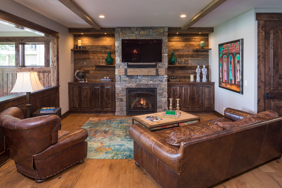 Photo of a rustic living room in Minneapolis with brown walls, medium hardwood flooring, a standard fireplace, a stone fireplace surround, a wall mounted tv and brown floors.