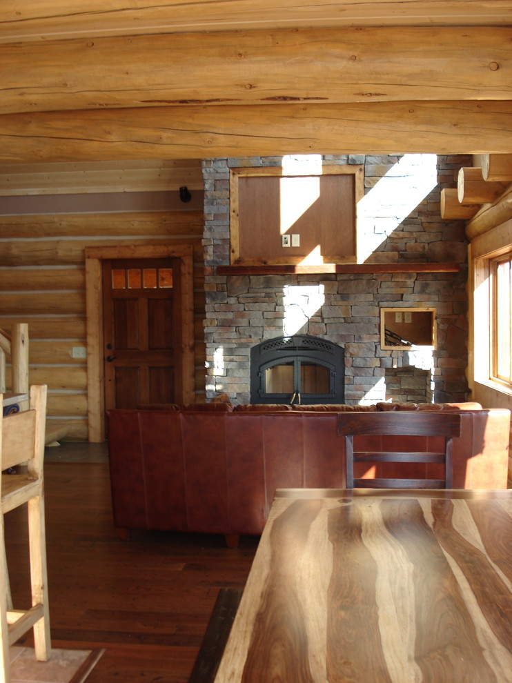 Foto de salón tipo loft de estilo americano de tamaño medio con paredes marrones, suelo de madera oscura, estufa de leña, marco de chimenea de piedra y televisor colgado en la pared
