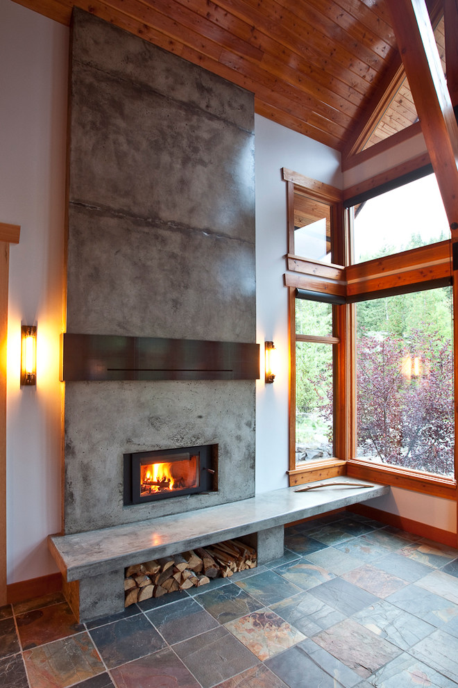 Cette photo montre un salon montagne ouvert avec un mur blanc, un sol en ardoise et un manteau de cheminée en béton.