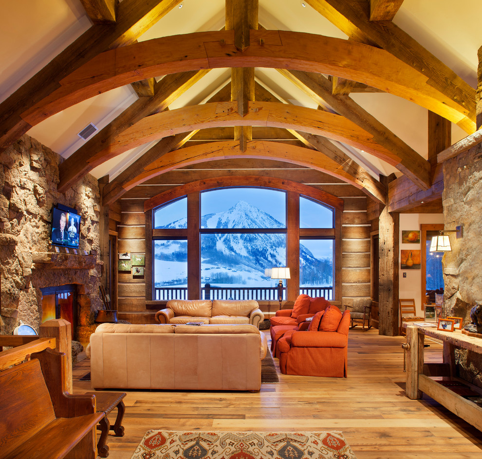 Cette image montre un salon chalet avec une salle de réception, un téléviseur fixé au mur, un sol en bois brun, une cheminée standard, un manteau de cheminée en pierre et éclairage.