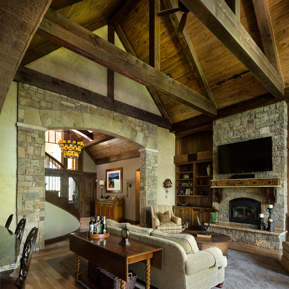Diseño de salón abierto rústico grande con suelo de madera clara, todas las chimeneas, marco de chimenea de piedra y televisor colgado en la pared