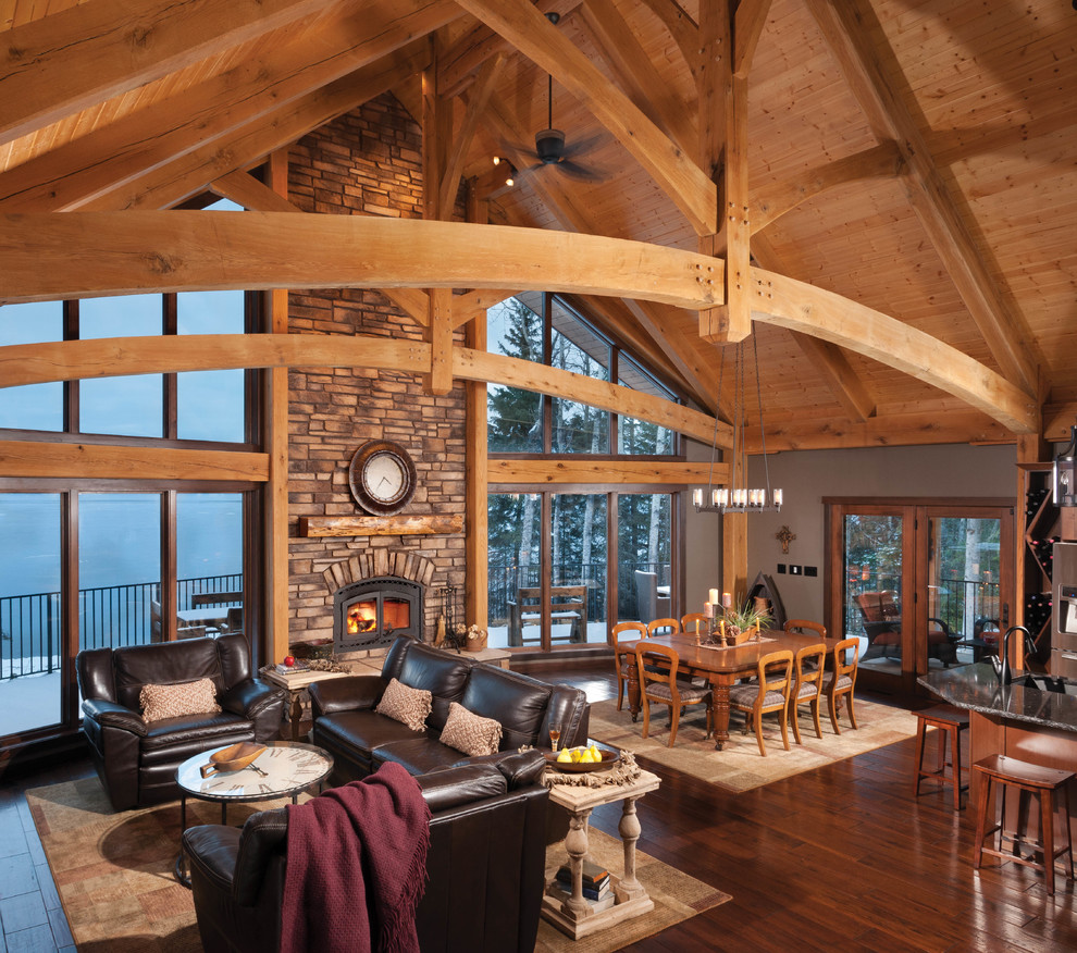 Large rustic open plan living room in Calgary with a stone fireplace surround, dark hardwood flooring, brown walls and a wood burning stove.