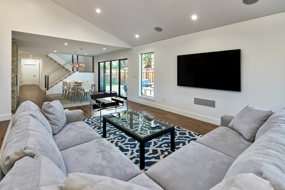 Diseño de salón abierto contemporáneo con paredes grises, suelo de madera en tonos medios, televisor colgado en la pared y suelo marrón