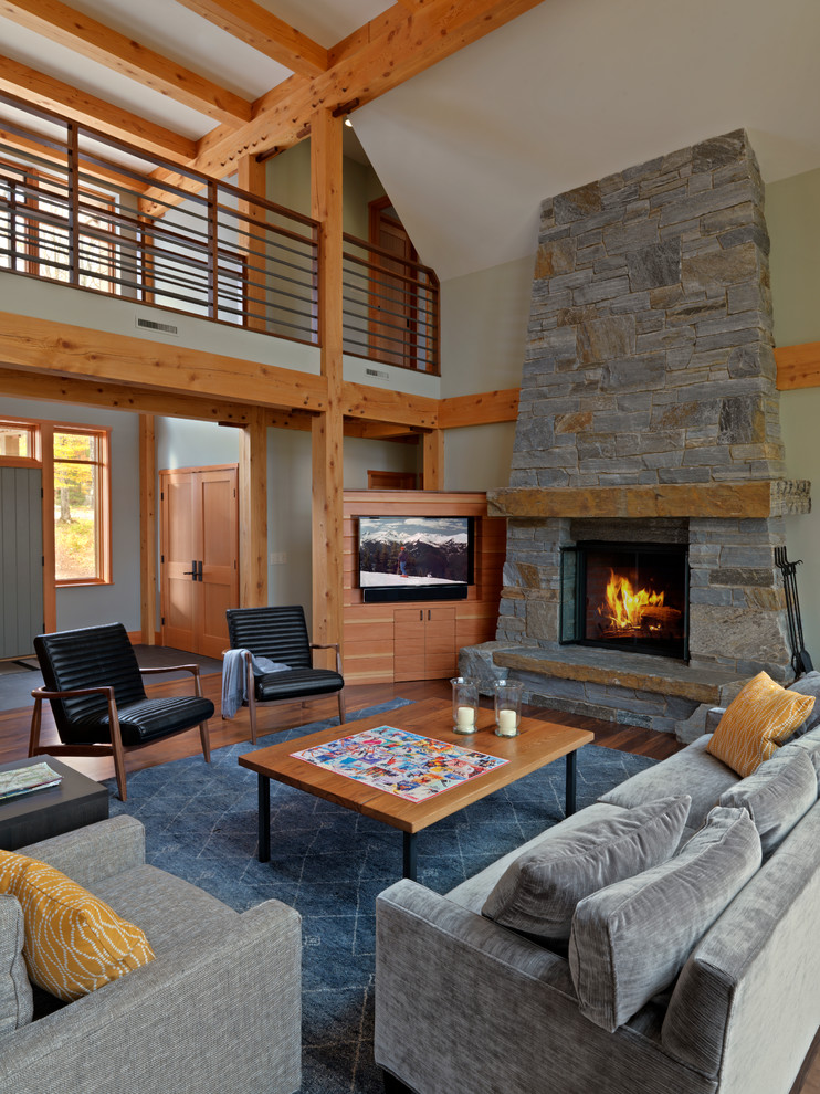 Cette photo montre un salon montagne ouvert avec un manteau de cheminée en pierre, un téléviseur encastré, un mur gris, parquet foncé et une cheminée standard.