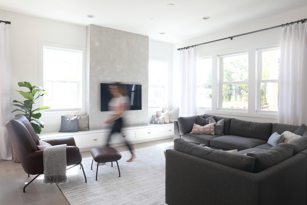 Modelo de salón abierto de estilo americano grande sin chimenea con paredes grises, suelo de madera en tonos medios, televisor colgado en la pared y suelo marrón
