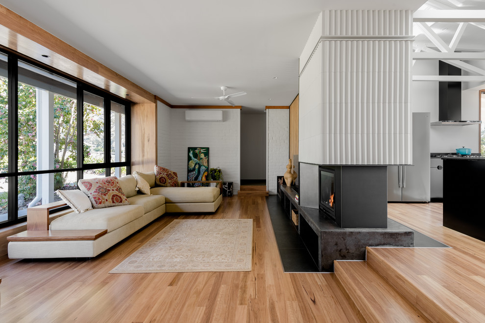 Aménagement d'un grand salon rétro ouvert avec un mur blanc, un sol en bois brun, une cheminée double-face, un manteau de cheminée en carrelage, un téléviseur indépendant et un sol marron.