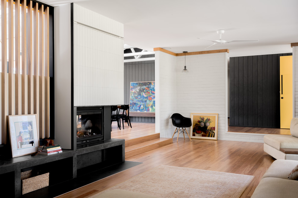 Immagine di un grande soggiorno minimalista aperto con pareti bianche, pavimento in legno massello medio, camino bifacciale, cornice del camino piastrellata e TV autoportante