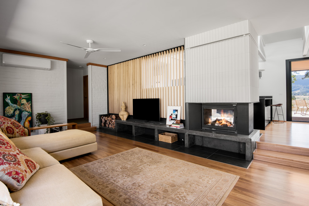 Large 1960s open concept medium tone wood floor living room photo in Other with white walls, a two-sided fireplace, a tile fireplace and a tv stand