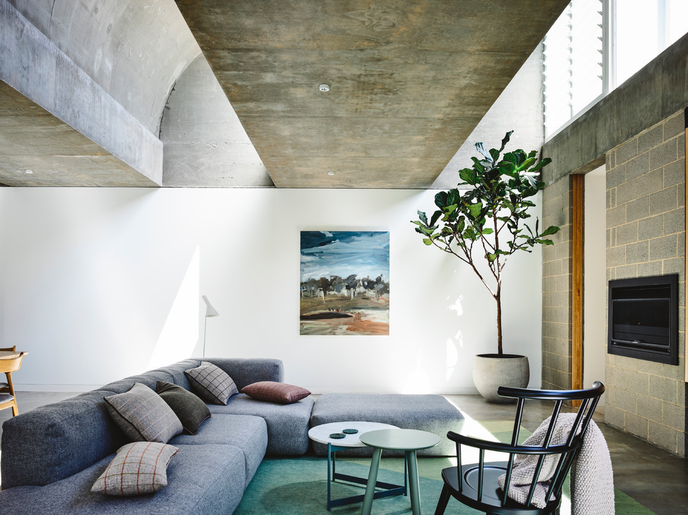 Modelo de salón abierto contemporáneo con paredes blancas, suelo de cemento, marco de chimenea de hormigón, televisor colgado en la pared y suelo gris