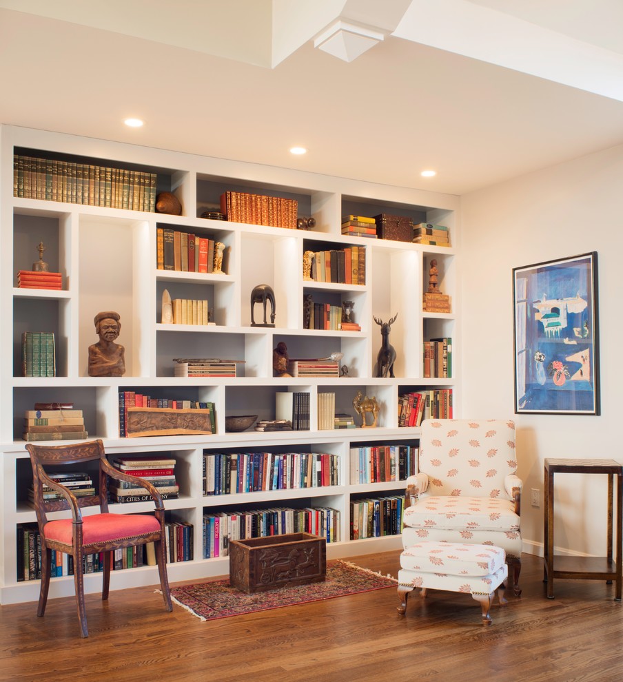 Ejemplo de biblioteca en casa abierta clásica renovada grande con paredes blancas, suelo de madera en tonos medios, todas las chimeneas, marco de chimenea de piedra y pared multimedia