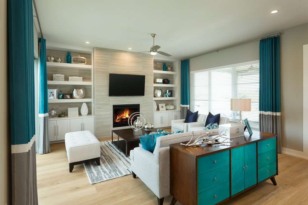 Пример оригинального дизайна: гостиная комната в стиле неоклассика (современная классика) с серыми стенами, стандартным камином, фасадом камина из плитки, светлым паркетным полом и синими шторами