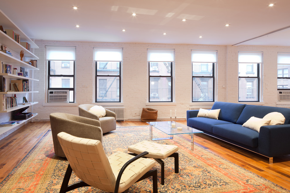 Immagine di un soggiorno contemporaneo con libreria, pareti bianche e pavimento in legno massello medio