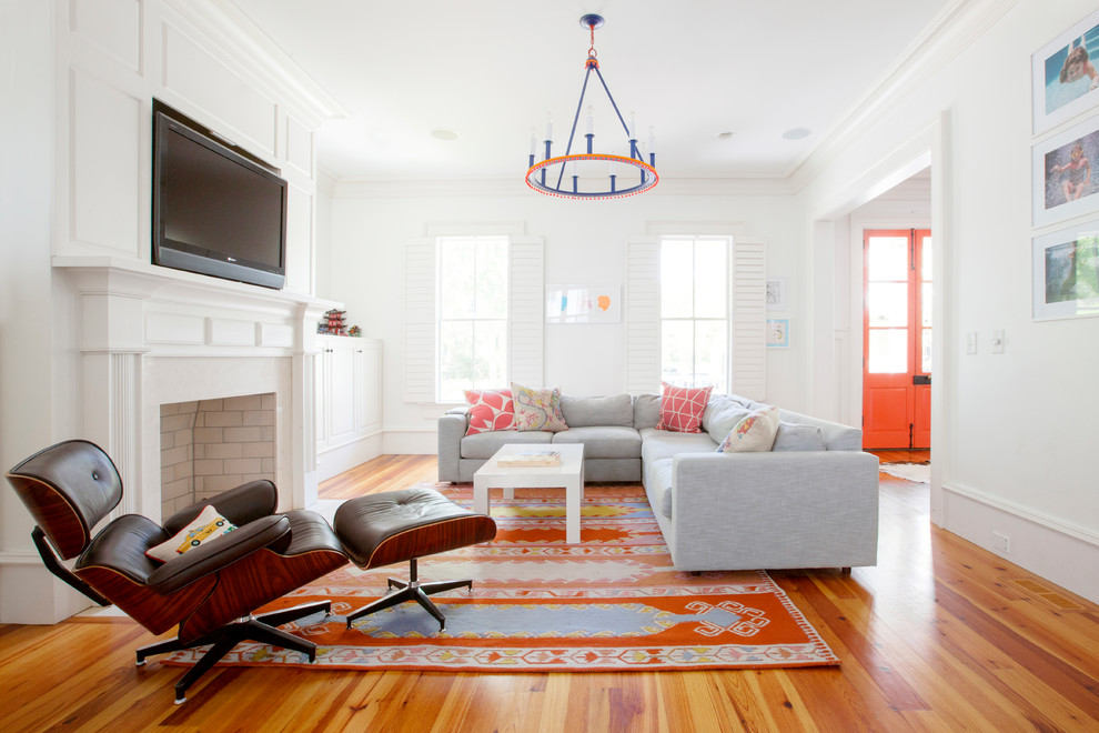 Repräsentatives, Abgetrenntes Eklektisches Wohnzimmer mit weißer Wandfarbe, braunem Holzboden, Kamin, Kaminumrandung aus Stein, TV-Wand und orangem Boden in Charleston