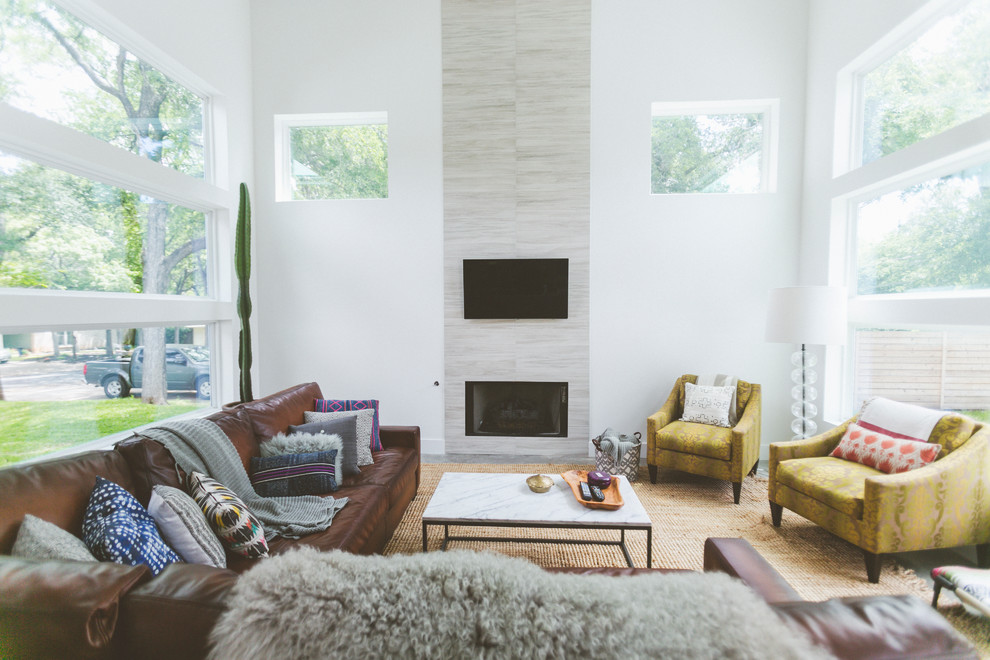 На фото: гостиная комната в современном стиле с белыми стенами, стандартным камином, фасадом камина из плитки, телевизором на стене и коричневым диваном с