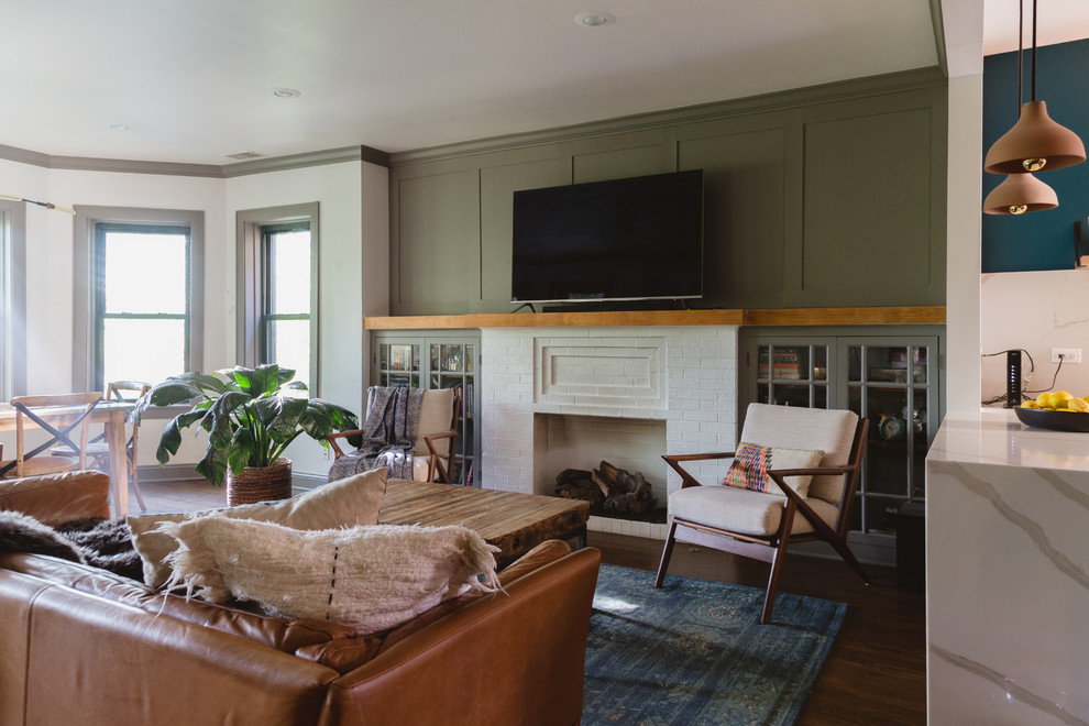 Foto på ett eklektiskt vardagsrum, med gröna väggar, mörkt trägolv, en standard öppen spis, en spiselkrans i tegelsten, en väggmonterad TV och brunt golv