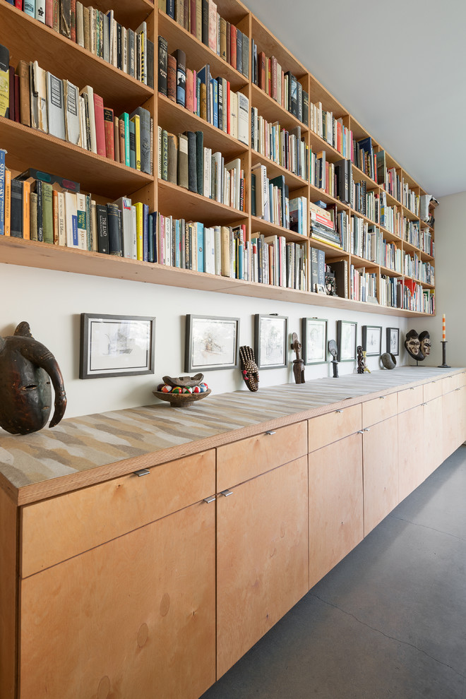 Cette image montre un salon design ouvert avec une bibliothèque ou un coin lecture, un mur blanc et sol en béton ciré.