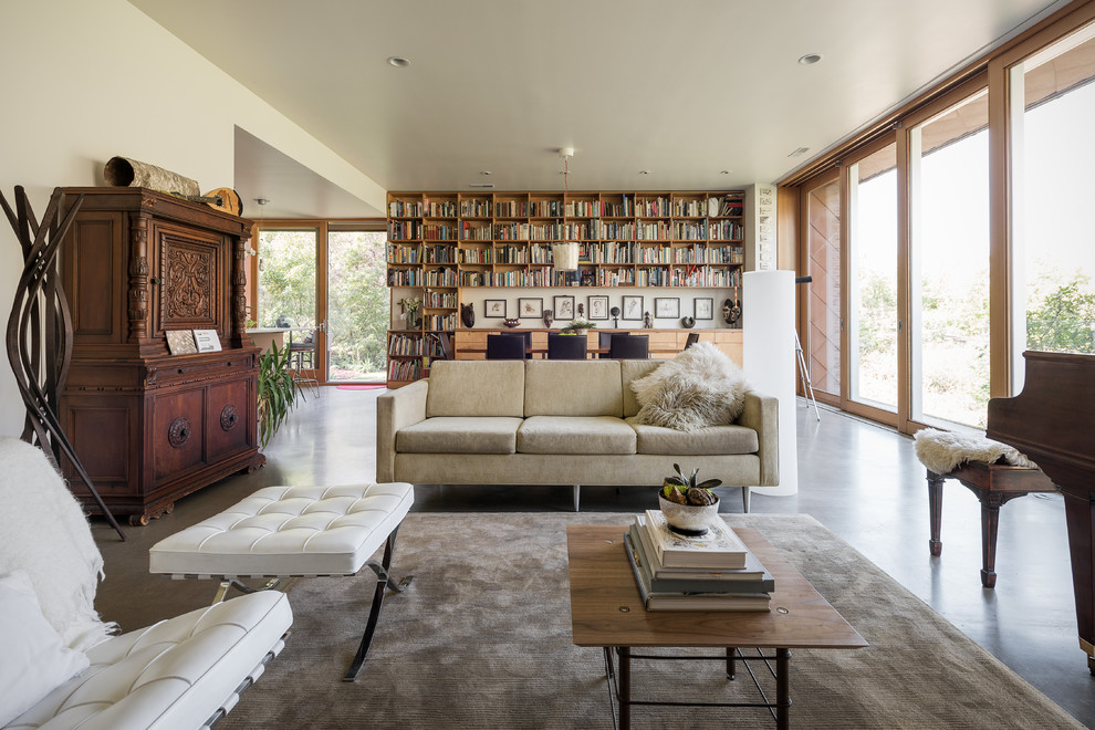 Стильный дизайн: открытая гостиная комната в стиле модернизм с с книжными шкафами и полками, белыми стенами и бетонным полом - последний тренд