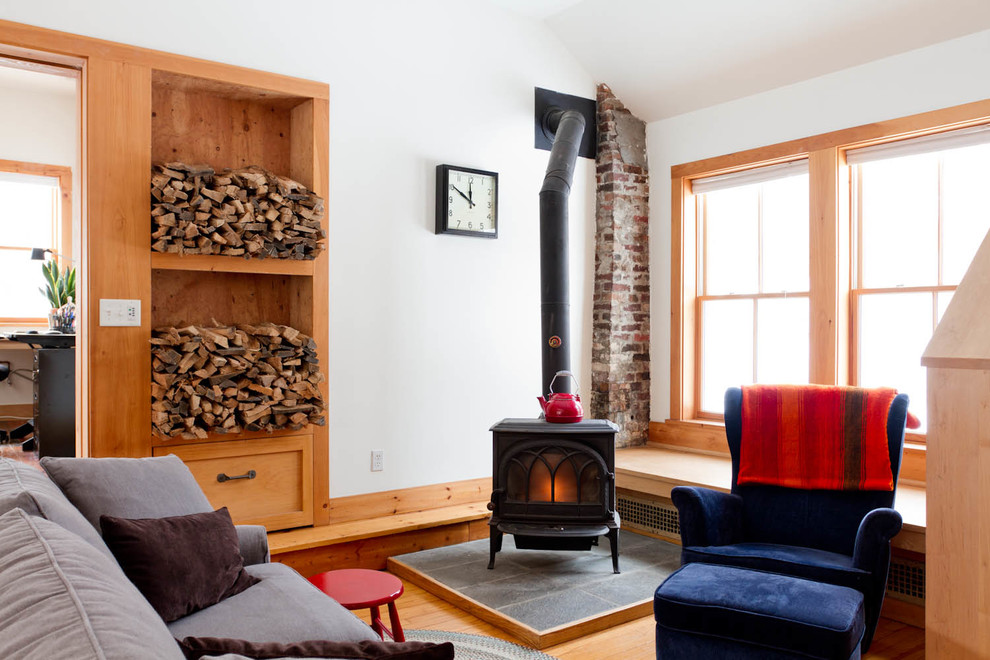 Example of an eclectic medium tone wood floor living room design in New York with white walls and a wood stove