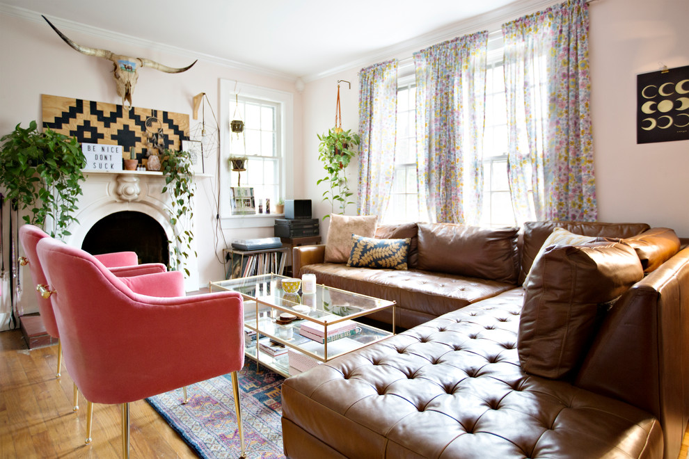 Источник вдохновения для домашнего уюта: изолированная гостиная комната в стиле фьюжн с розовыми стенами, паркетным полом среднего тона, стандартным камином, фасадом камина из штукатурки, телевизором на стене и коричневым полом