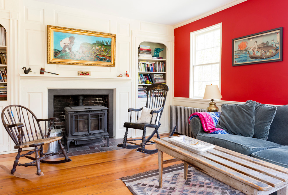 Example of an eclectic medium tone wood floor living room library design in Portland Maine with red walls and a wood stove