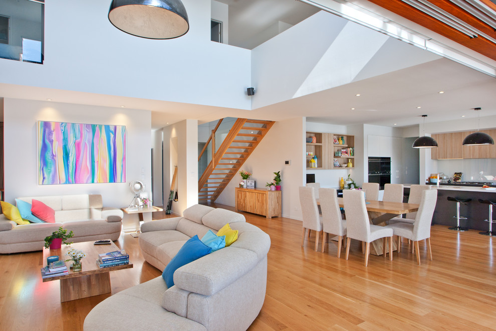 Cette image montre un salon design ouvert avec un mur blanc et un sol en bois brun.