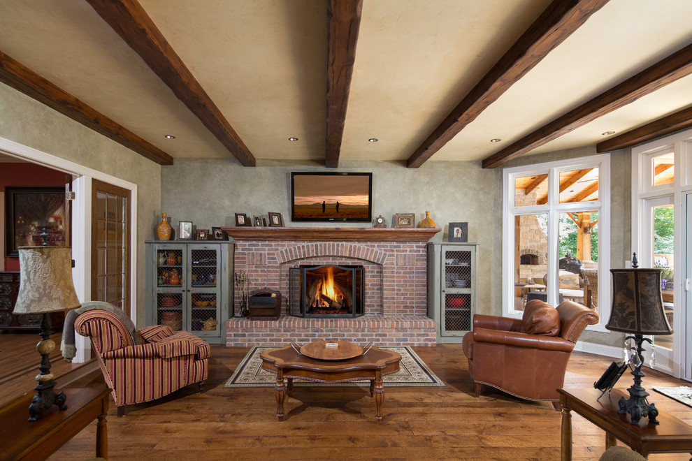 Inspiration pour un grand salon traditionnel fermé avec un sol en bois brun, une cheminée standard, un manteau de cheminée en brique, une salle de réception, un mur gris et un téléviseur fixé au mur.