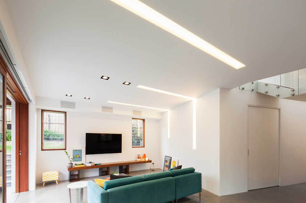 Пример оригинального дизайна: открытая гостиная комната в современном стиле с белыми стенами, бетонным полом и телевизором на стене без камина