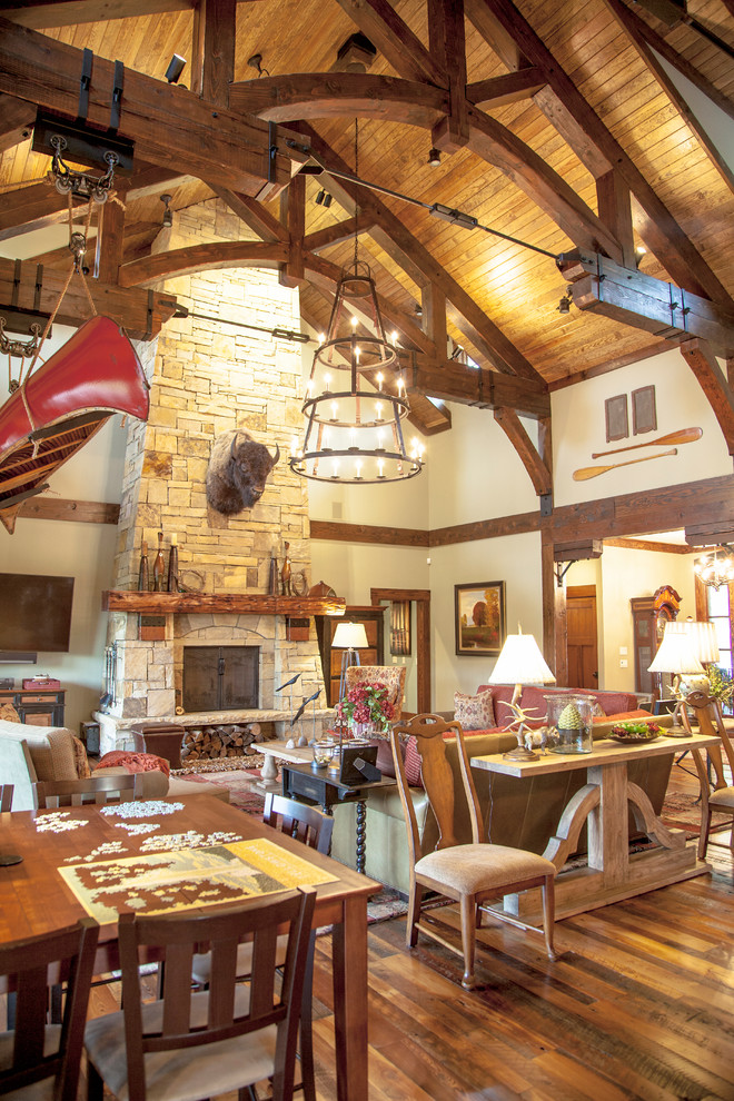 Example of a large mountain style formal and open concept medium tone wood floor and brown floor living room design in Other with beige walls, a standard fireplace, a stone fireplace and a wall-mounted tv