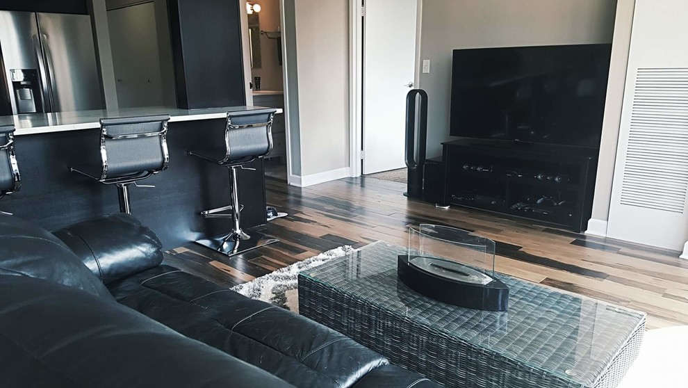 Modelo de salón abierto moderno de tamaño medio con paredes grises, suelo de madera en tonos medios, chimenea de doble cara, televisor independiente y suelo multicolor