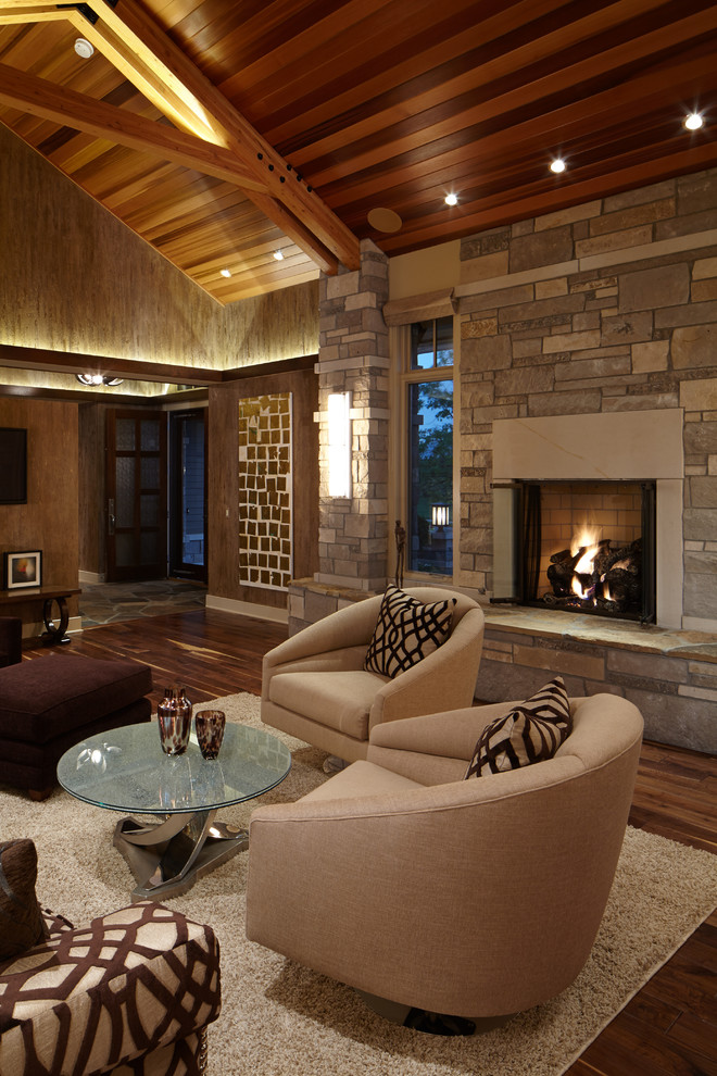 На фото: большая открытая гостиная комната в стиле кантри с коричневыми стенами, паркетным полом среднего тона, стандартным камином и фасадом камина из камня
