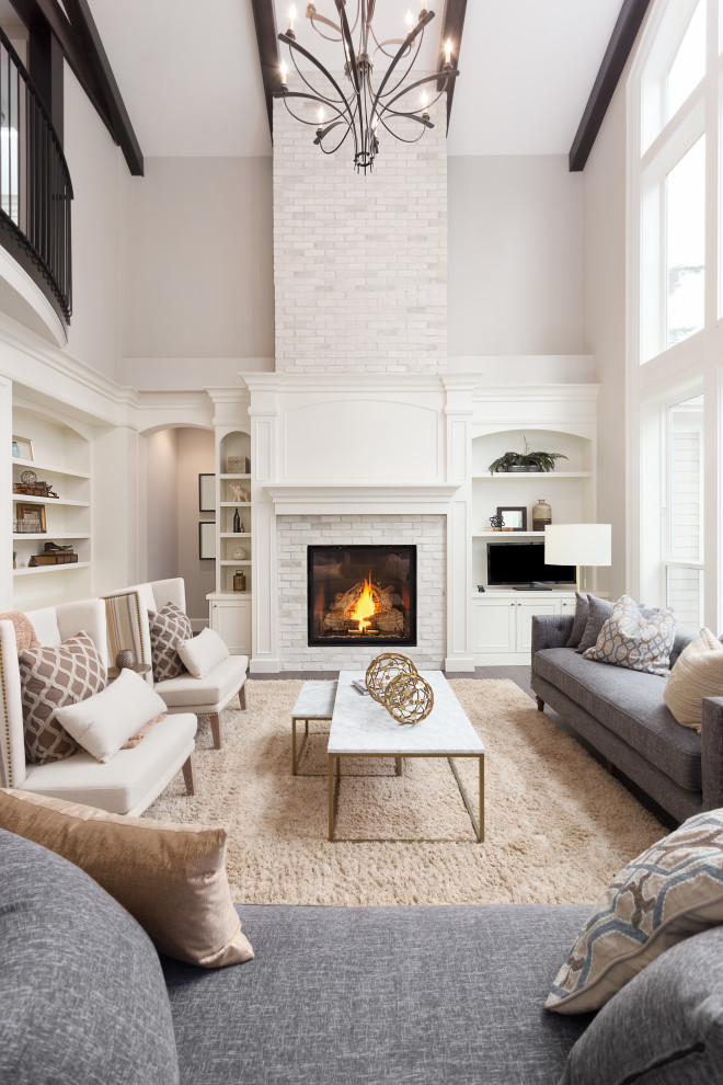 Expansive classic open plan living room in New York with grey walls, dark hardwood flooring, a standard fireplace, a brick fireplace surround, a built-in media unit, brown floors and exposed beams.
