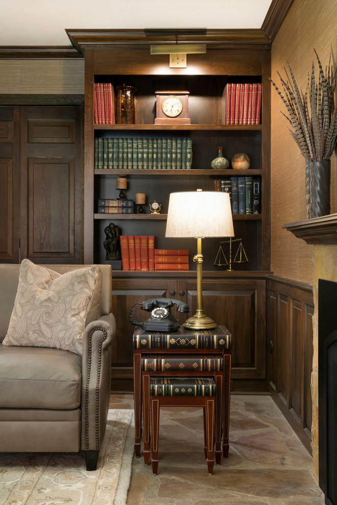 Bild på ett mellanstort vintage separat vardagsrum, med ett bibliotek, beige väggar, kalkstensgolv, en standard öppen spis, en spiselkrans i sten, en väggmonterad TV och flerfärgat golv
