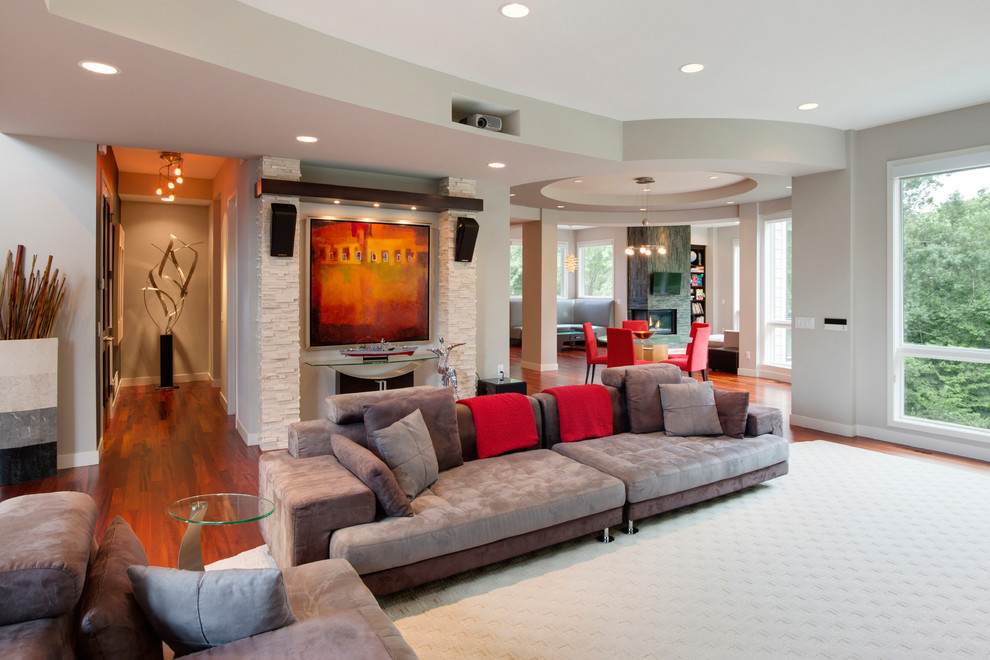 Imagen de salón abierto contemporáneo de tamaño medio con paredes grises, suelo de madera en tonos medios y televisor colgado en la pared