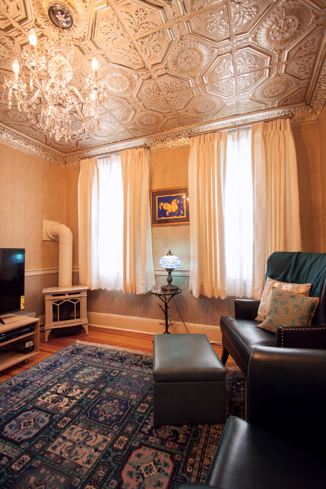 Cette image montre un petit salon traditionnel fermé avec une bibliothèque ou un coin lecture, un mur beige, un sol en bois brun, un poêle à bois, un manteau de cheminée en métal, un téléviseur indépendant et un sol bleu.