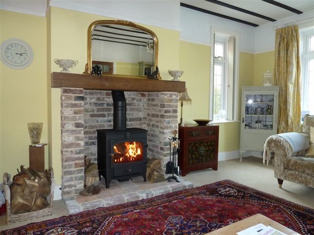 На фото: гостиная комната в стиле шебби-шик с печью-буржуйкой и фасадом камина из кирпича с