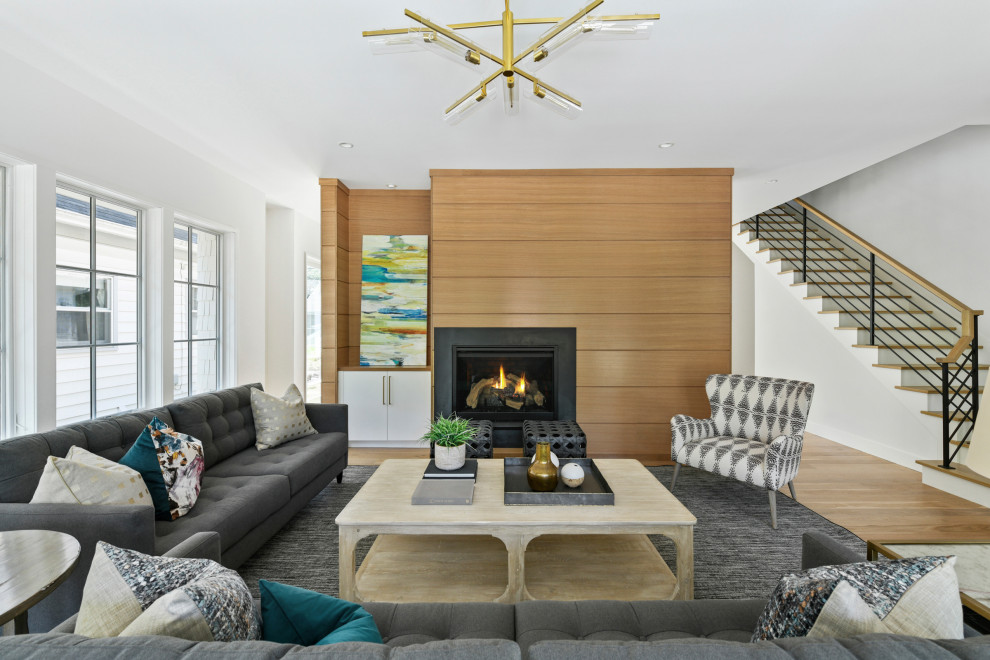 Пример оригинального дизайна: большая гостиная комната в стиле неоклассика (современная классика) с белыми стенами, светлым паркетным полом, стандартным камином, фасадом камина из дерева и деревянными стенами без телевизора