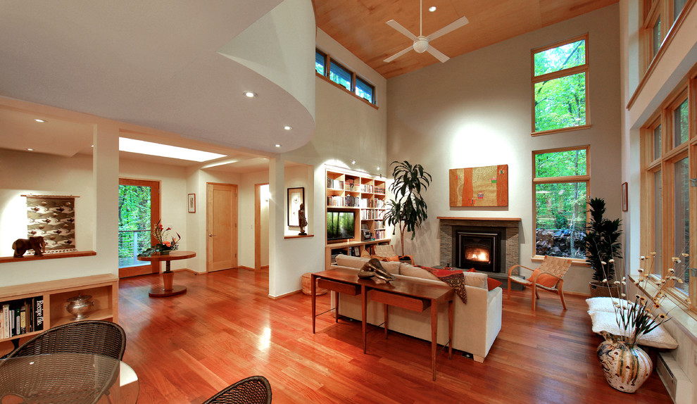 Exemple d'un salon tendance ouvert avec un mur blanc, un sol en bois brun, une cheminée standard, un manteau de cheminée en pierre et un téléviseur encastré.