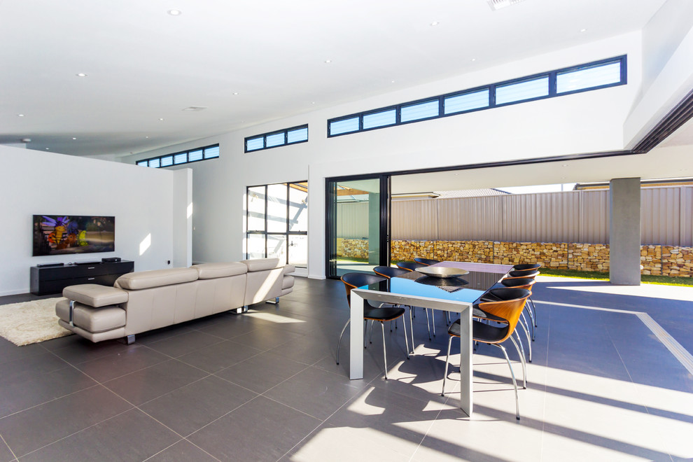 Пример оригинального дизайна: большая открытая гостиная комната в стиле модернизм с белыми стенами, полом из керамической плитки и телевизором на стене